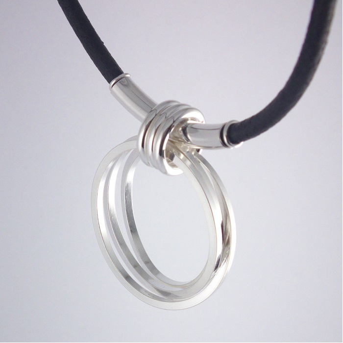 Halssmycke, en tre-varvad ring, ca 4 cm i diameter, häger i en läderrem.